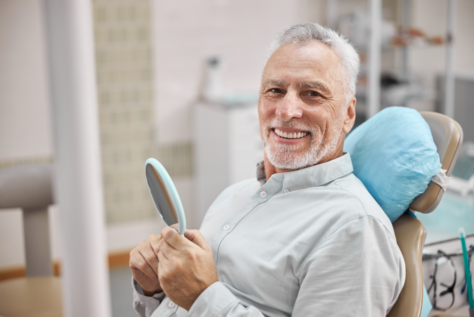 Smiling man holding a mirror at dentist.